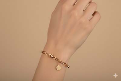 Gold bracelet with a small round charm on a wrist against a beige background