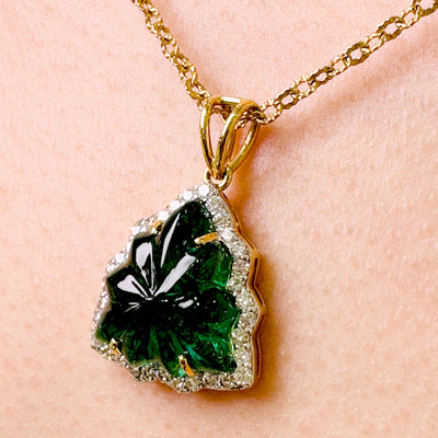 A close up view of tresor collection's carved emerald leaf cut pendant studded with diamonds in 18kt Yellow gold