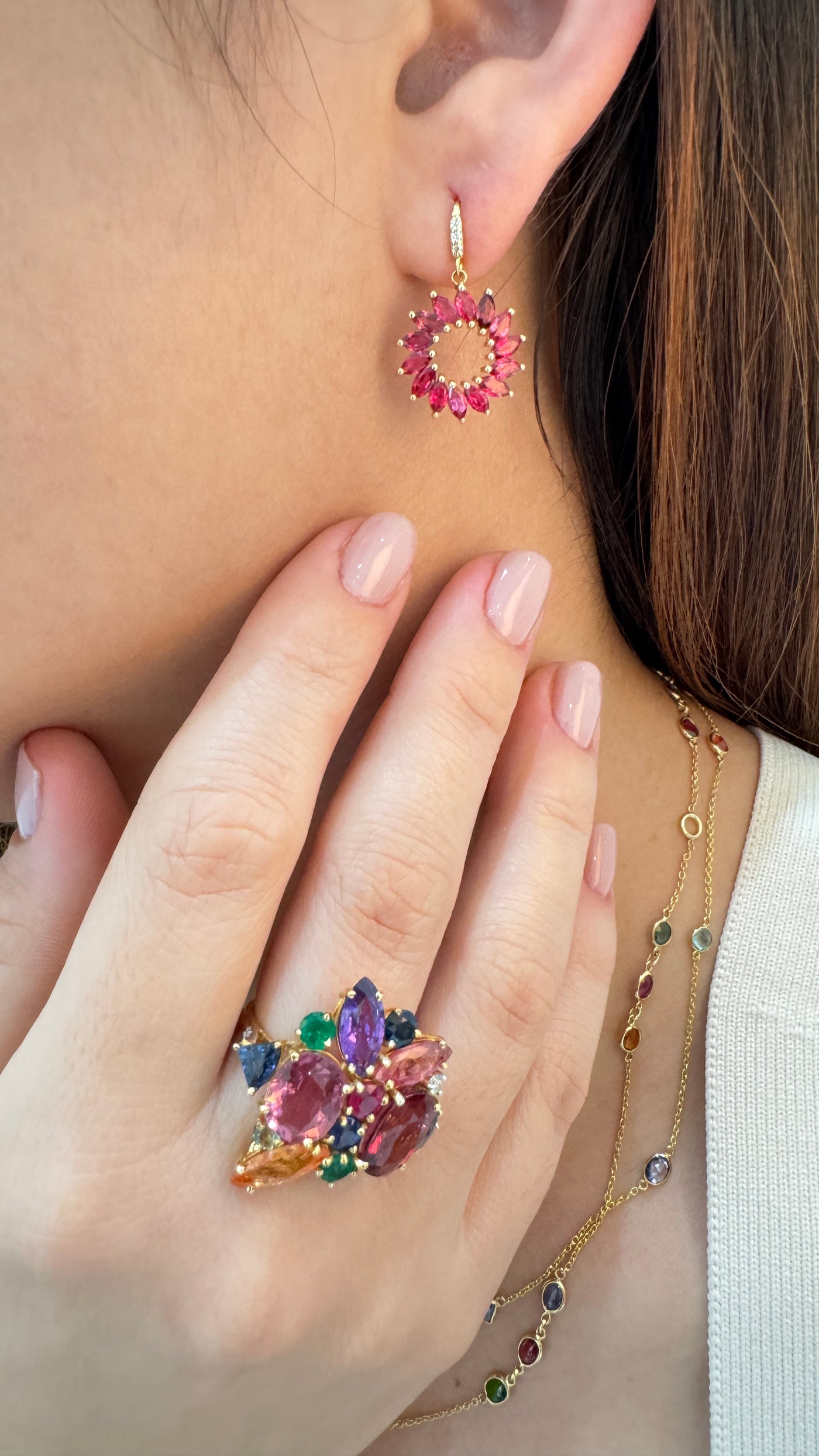 Close-up of a person wearing colorful gemstone earrings and a ring.
