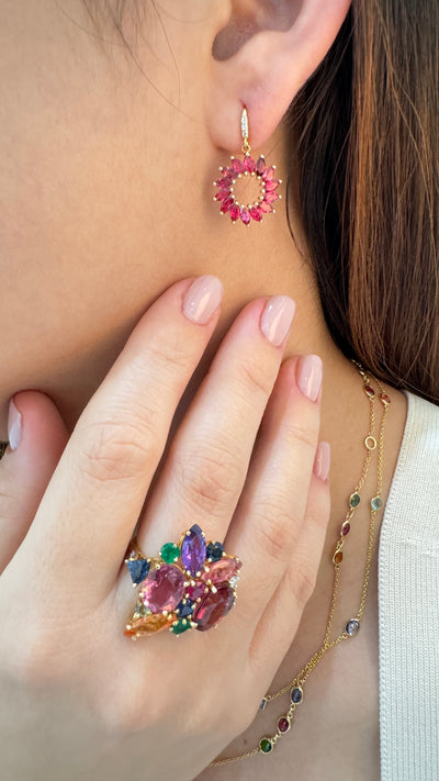 Close-up of a person wearing colorful gemstone earrings and a ring.