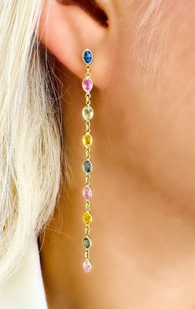 Multi Sapphire Oval Earring In 18K Yellow Gold - Tresor Collection Close-up of model wearing gold multi-color sapphire drop earrings – radiant handcrafted gemstone design