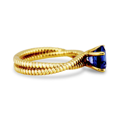 Tanzanite Round Ring In 18K Yellow Gold - Tresor Collection Person adjusting the gold tanzanite ring on their finger – focusing on the intricate details of the ring.