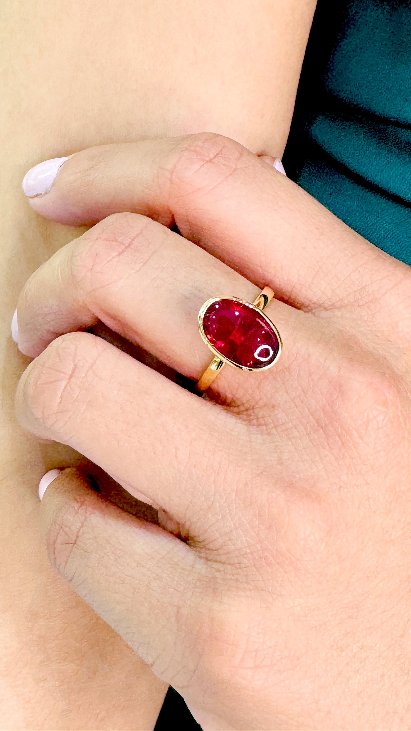 Gold ring with a red gemstone on a person's finger Oval orange sapphire ring on model’s hand – statement 18K gold gemstone jewelry by Tresor Collection