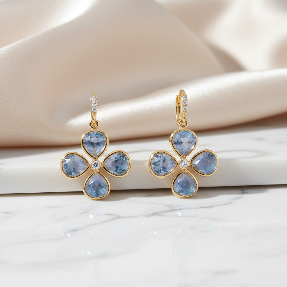 Gold earrings with blue gemstones on a soft fabric background Gold clover earrings with blue gemstones displayed on marble and satin – sophisticated jewelry styling