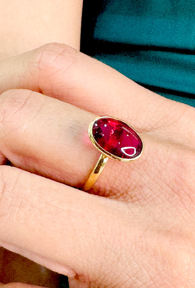 Gold ring with a red gemstone on a person's finger Gold ring with oval pink tourmaline styled on model – vibrant gemstone statement ring