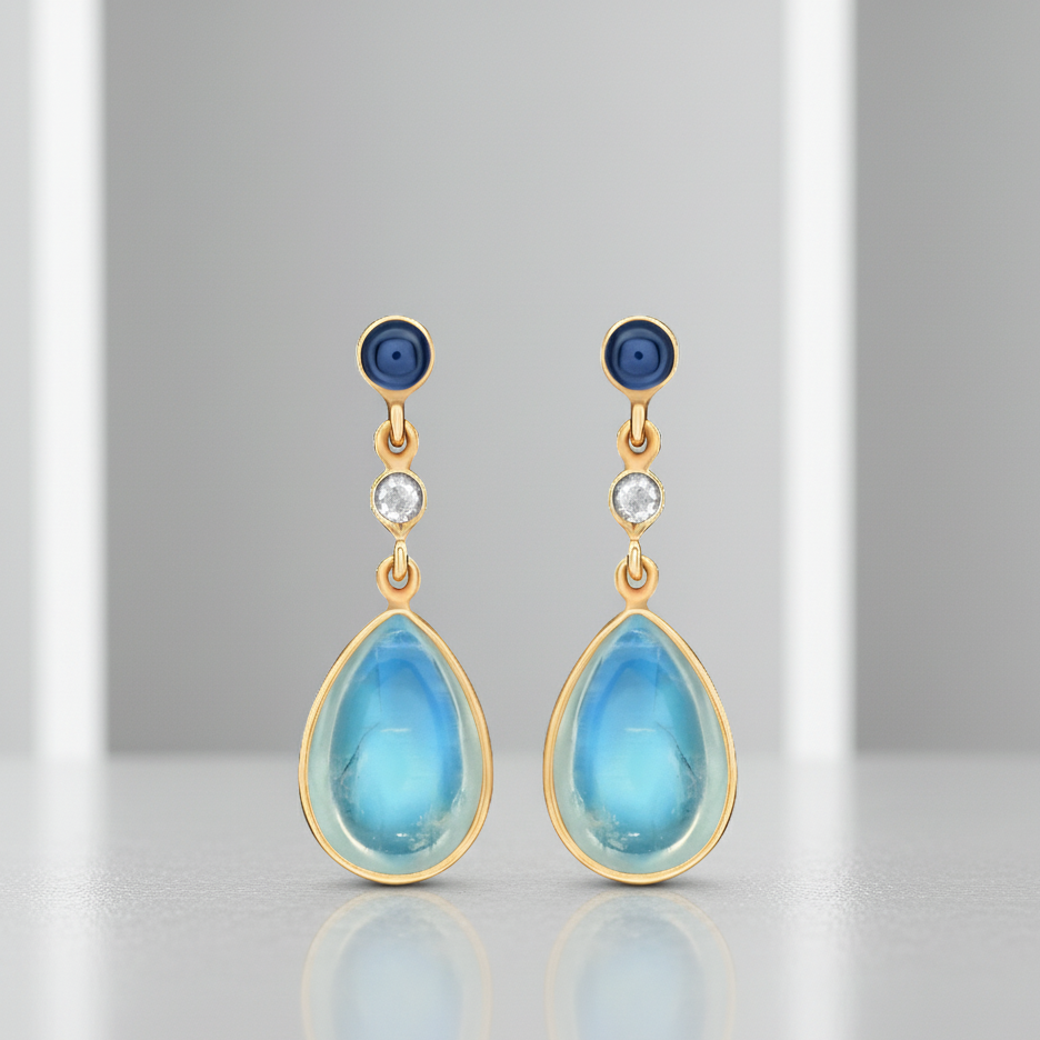 Teardrop-shaped earrings with blue stones and gold accents on a gray background Pair of Rainbow Moonstone and Blue Sapphire teardrop earrings – artisan-crafted gemstone jewelry in gold