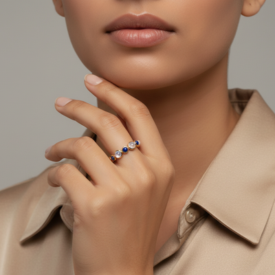 Close-up of a hand wearing a ring with colored gemstones, set against a neutral background.