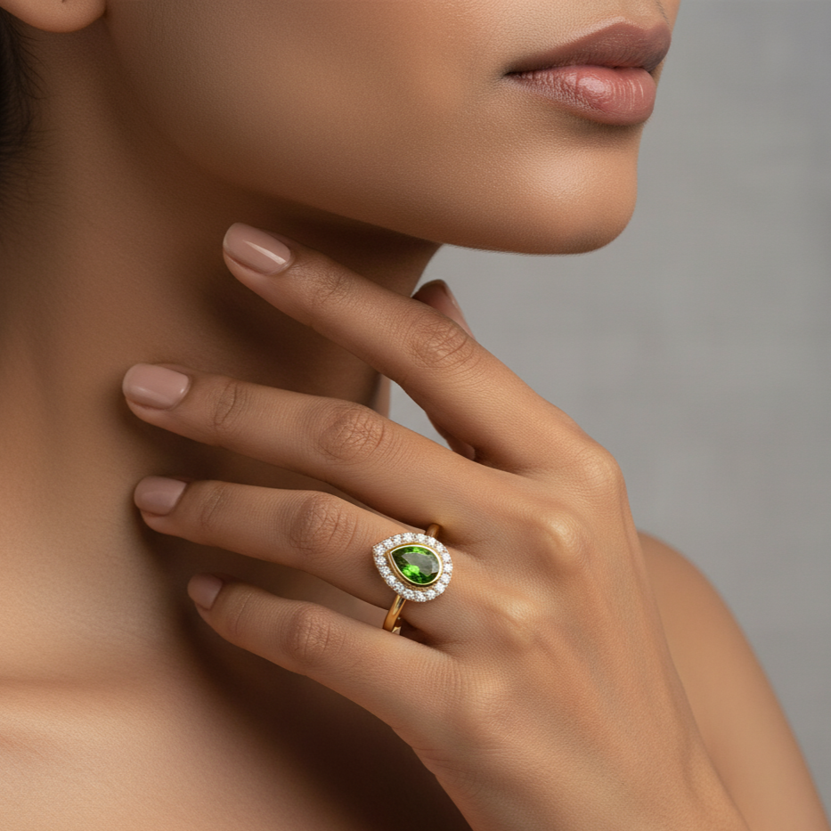 Close-up of a hand wearing a gold ring with a green gemstone on a neutral background
