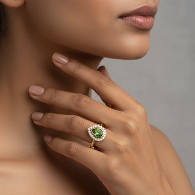 Close-up of a hand wearing a gold ring with a green gemstone on a neutral background