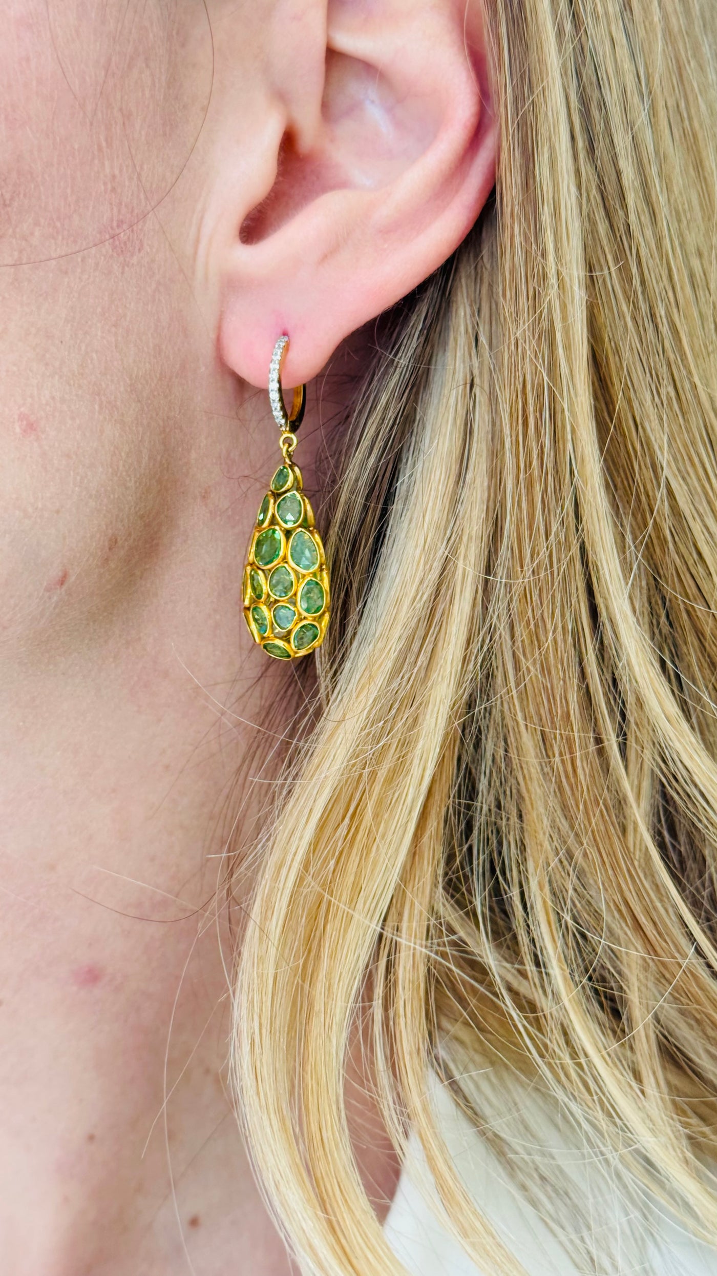Close-up of a person wearing gold earrings with green gemstones. Close-up of green gemstone drop earrings on model – luxury handcrafted gold earrings