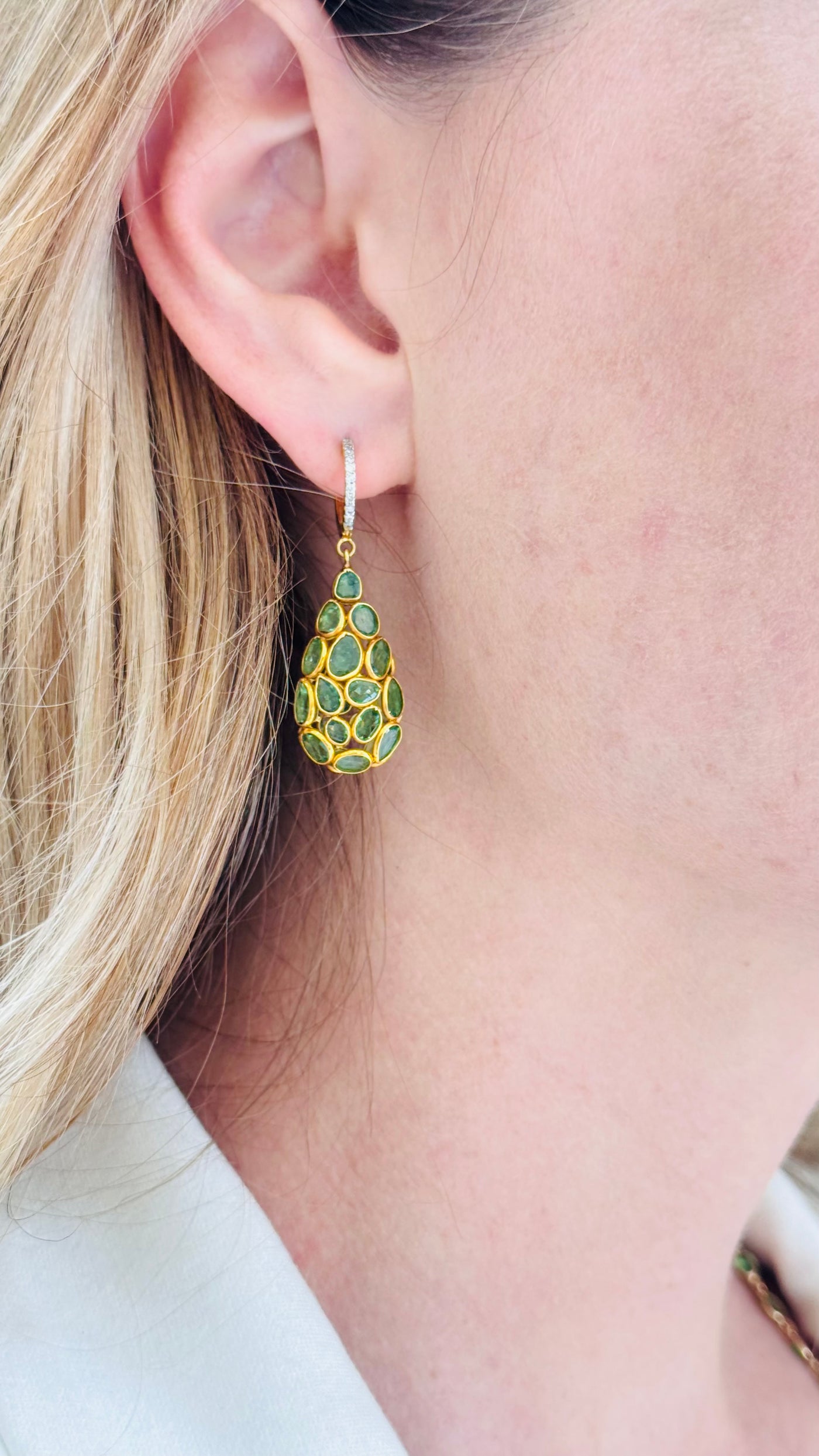 Gold earrings with green gemstones worn by a person with blonde hair. Side view of model wearing green gemstone drop earrings – modern handcrafted jewelry