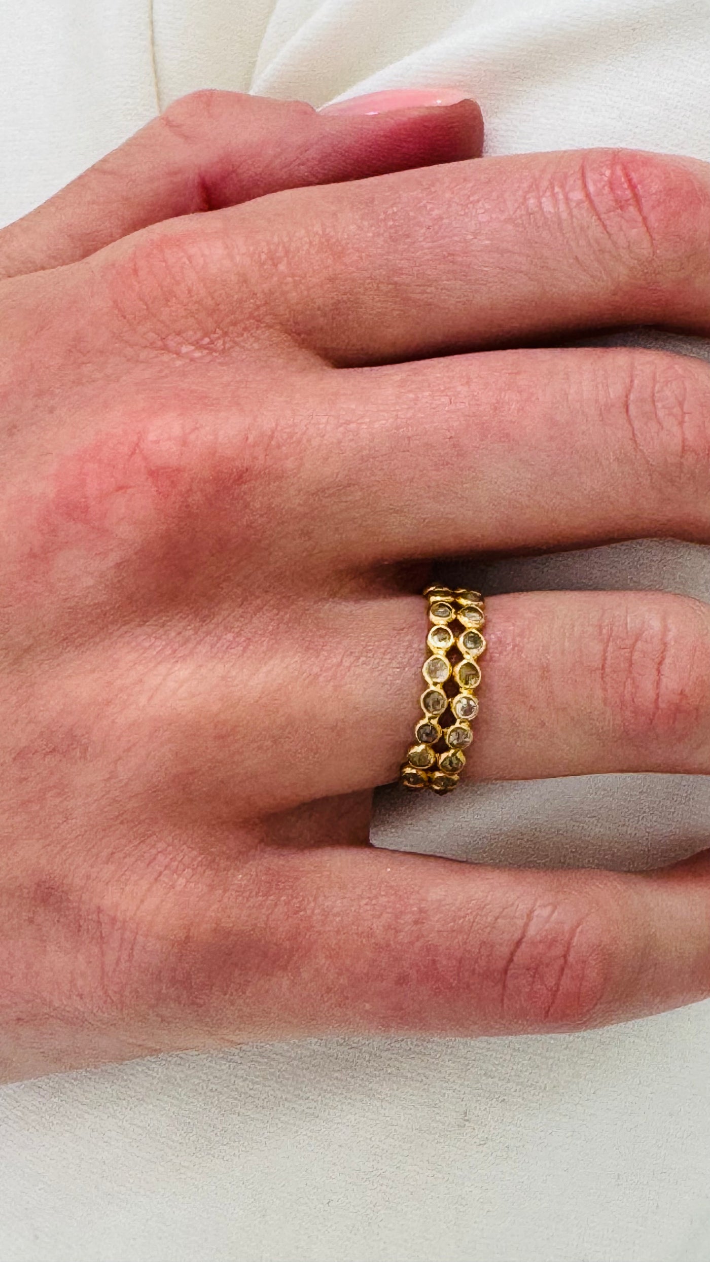 Gold ring on a person's finger against a white background Close-up of 18K yellow gold diamond band ring worn on hand – elegant everyday fine jewelry