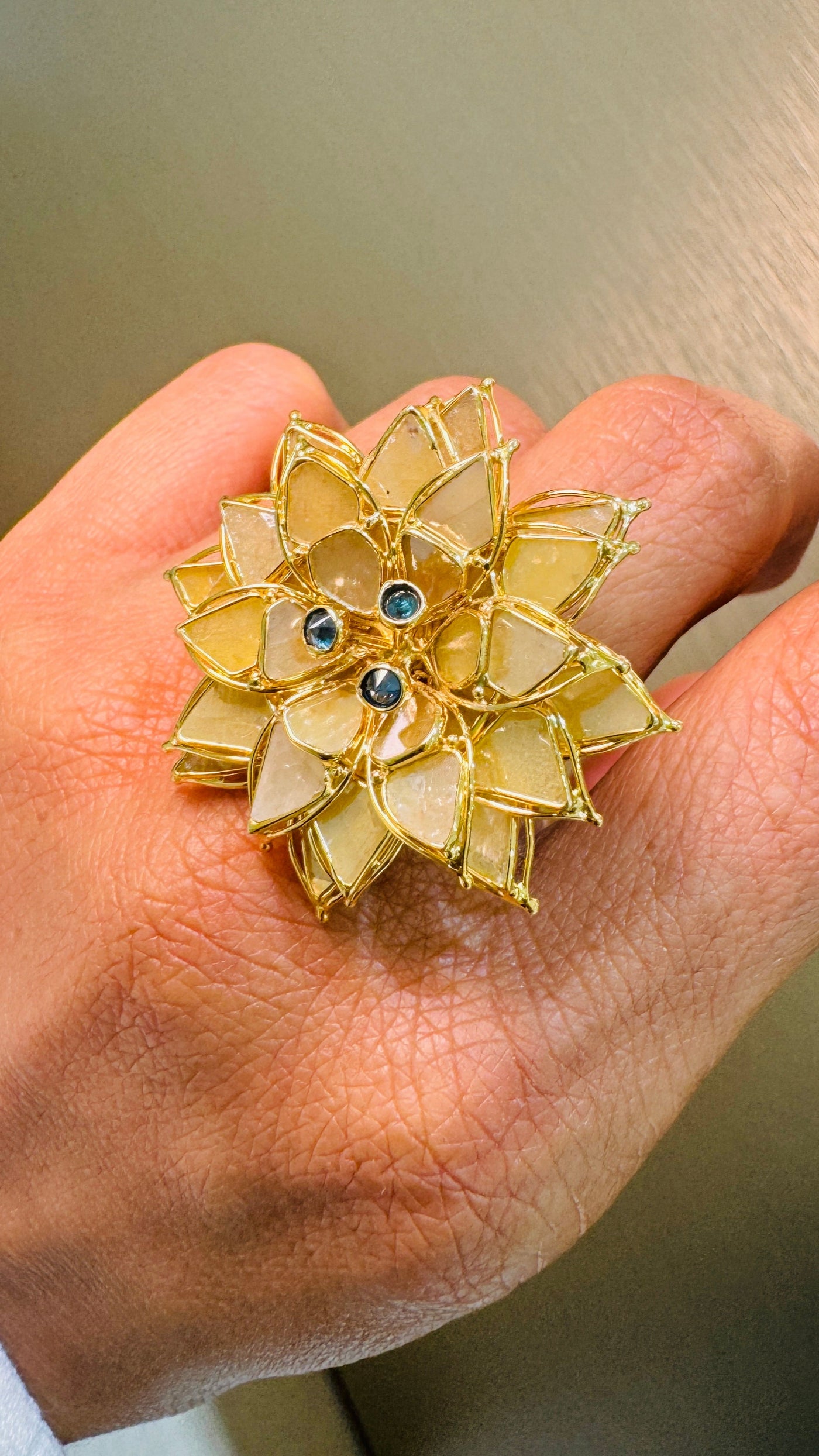 Close-up of floral ring on finger – detailed 18K yellow gold craftsmanship with blue center stones by Tresor Collection