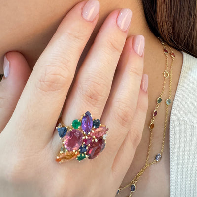 Close-up of a person wearing colorful gemstone earrings and a ring. Multicolor gemstone ring styled for festive occasion – luxury handcrafted jewelry from Tresor Collection