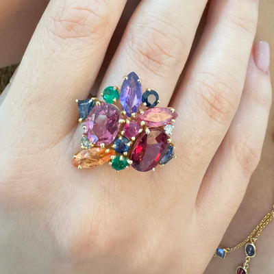 Multicolored gemstone ring on a hand with matching earrings. Elegant multicolor gemstone ring on model’s hand – designer gold jewelry for women by Tresor Collection