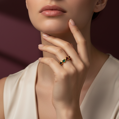 Close-up of a woman's hand wearing a ring with colored gemstones against a neutral background Elegant emerald ruby sapphire gold ring on model – designer jewelry for women by Tresor Collection