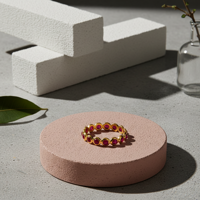 Gold ring with red stones on a pink stand with a concrete background Close-up of 18K gold ruby ring – handcrafted gemstone jewelry from Tresor Collection