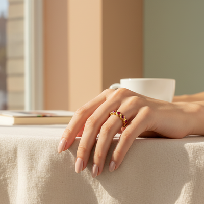 Hand wearing a gold ring with red stones on a light surface, blurred background Ruby gold ring styled for festive occasions – luxury handcrafted jewelry from Tresor Collection