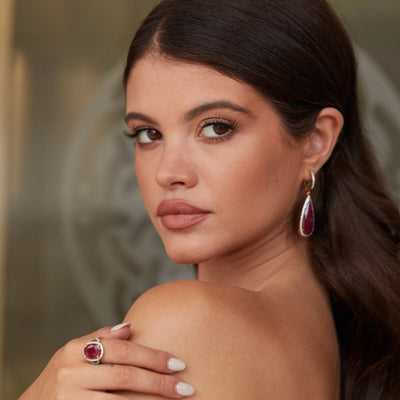 Angled view of model wearing ruby and diamond teardrop earrings in 18k yellow gold – Tresor Collection jewelry Close-up of pear-shaped cabochon ruby earrings in 18K gold – bespoke fine jewelry craftsmanship