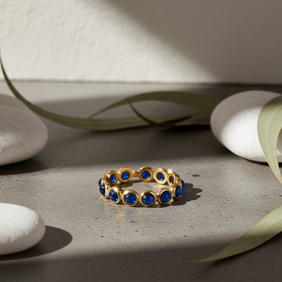 Gold ring with blue stones on a stone surface with leaves Close-up of 18K gold blue sapphire cabochon ring – handcrafted fine jewelry from Tresor Collection boutique
