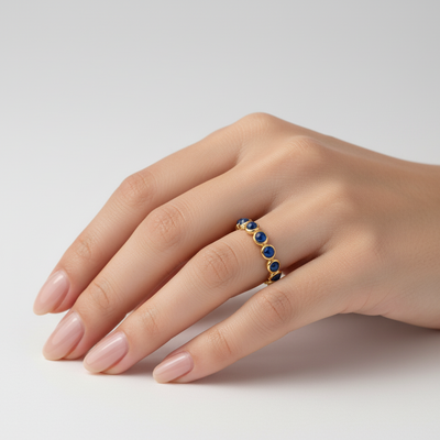 Gold ring with blue stones on a hand against a light gray background Blue sapphire gold ring styled for daily elegance – luxury handcrafted jewelry from Tresor Collection