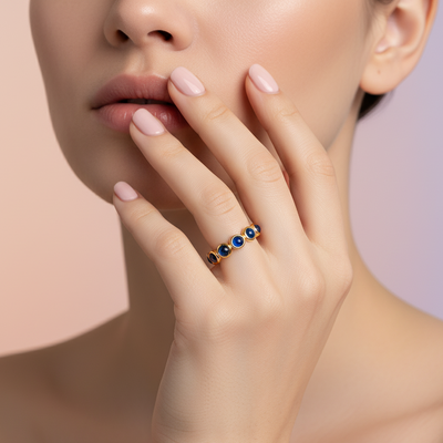 Close-up of a hand wearing a ring with blue stones on a neutral de24410bs-ring-on-model.jpg background