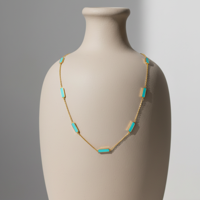Necklace with turquoise stones on a beige vase against a gray background Close-up of 18K gold turquoise necklace – handcrafted gemstone jewelry from Tresor Collection boutique