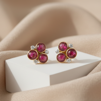 Pair of gemstone earrings on a beige surface with a white stand. Close-up of 18K gold ruby and diamond earrings – handcrafted fine jewelry from Tresor Collection boutique