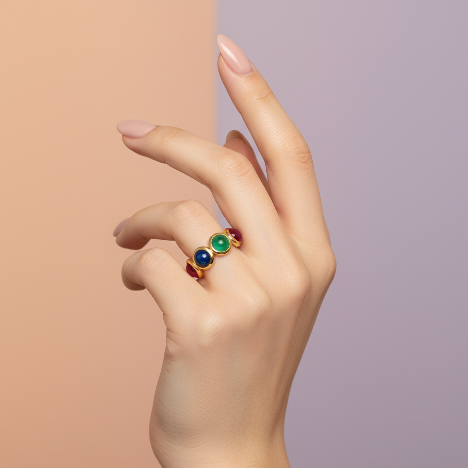 Hand wearing a ring with colorful gemstones on a gradient background Elegant emerald, ruby & sapphire gold ring on model – designer gemstone jewelry for women by Tresor Collection